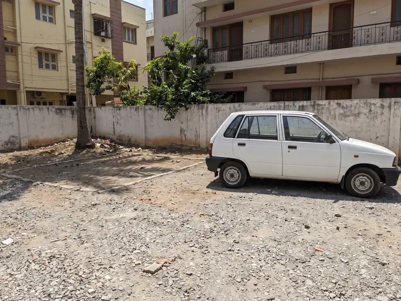 White hatchback parked in a walled gravel plot beside apartment buildings